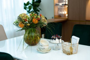 Cam bir sehpanın üzerinde, içinde bir vazo çiçek ve modern tasarım bir çay seti olan nefis bir çilekli pasta. Yumuşak seçici odak, sanat gürültüsü