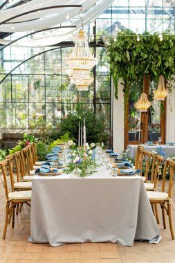 Mavi peçeteli ziyafet masası takımı, altın çatal bıçak takımı, kristal, taze çiçekler ve mumlar. Düğün süslemeleri. Yumuşak seçici odak.