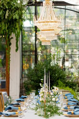 Mavi peçeteli ziyafet masası takımı, altın çatal bıçak takımı, kristal, taze çiçekler ve mumlar. Düğün süslemeleri. Yumuşak seçici odak.