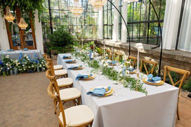 Mavi peçeteli ziyafet masası takımı, altın çatal bıçak takımı, kristal, taze çiçekler ve mumlar. Düğün süslemeleri. Yumuşak seçici odak.