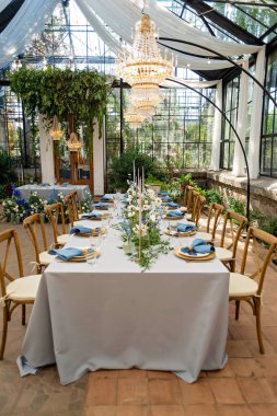 Mavi peçeteli ziyafet masası takımı, altın çatal bıçak takımı, kristal, taze çiçekler ve mumlar. Düğün süslemeleri. Yumuşak seçici odak.