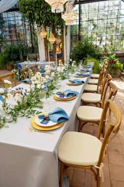 Mavi peçeteli ziyafet masası takımı, altın çatal bıçak takımı, kristal, taze çiçekler ve mumlar. Düğün süslemeleri. Yumuşak seçici odak.