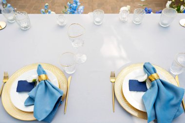 Altın, mavi renkler ve taze çiçeklerle süslenmiş zarif ve şık bir düğün masası. Yumuşak seçici odak.