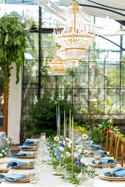 Mavi peçeteli ziyafet masası takımı, altın çatal bıçak takımı, kristal, taze çiçekler ve mumlar. Düğün süslemeleri. Yumuşak seçici odak.