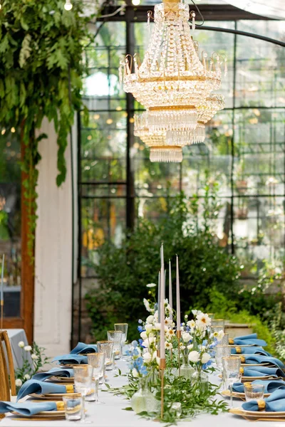 Mavi peçeteli ziyafet masası takımı, altın çatal bıçak takımı, kristal, taze çiçekler ve mumlar. Düğün süslemeleri. Yumuşak seçici odak.