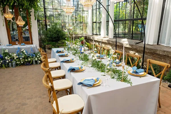 Mavi peçeteli ziyafet masası takımı, altın çatal bıçak takımı, kristal, taze çiçekler ve mumlar. Düğün süslemeleri. Yumuşak seçici odak.