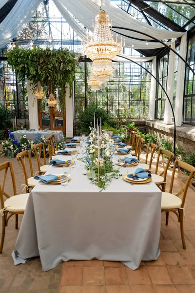 Mavi peçeteli ziyafet masası takımı, altın çatal bıçak takımı, kristal, taze çiçekler ve mumlar. Düğün süslemeleri. Yumuşak seçici odak.