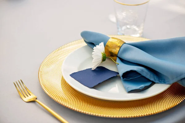 Altın, mavi renkler ve taze çiçeklerle süslenmiş zarif ve şık bir düğün masası. Yumuşak seçici odak.