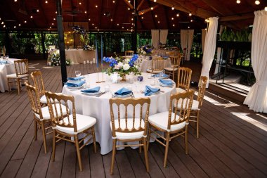 Şenlikli düğün, mavi keten peçeteler, mumlar, altın koltuklar ve taze çiçek buketleri. Düğün süslemeleri. Restoran menüsü konsepti. Yumuşak seçici odak.