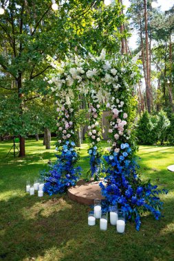 Yeşil bir çimenlikte açık havada düğün töreni. Beyaz ve mavi taze çiçeklerden yapılmış bir düğün için kemer. Yumuşak seçici odak.