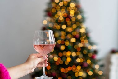 Bir kadeh şampanya, Noel ağacının arka planında el ele yükseldi. Kış tatili Yeni yıl geçmişi. Yumuşak seçici odak.