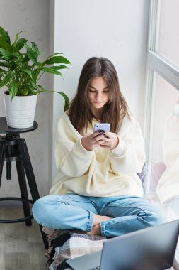 Akıllı telefona bakan, evde dinlenen, cep telefonu uygulamalarını kullanan, cep telefonuyla oyun oynayan, mesajları ya da sosyal medya mesajlarını kontrol eden mutlu genç kız. Yumuşak seçici odak.