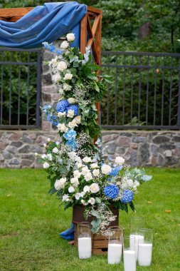 Açık havada düğün için bir yer. Mavi kumaş, çiçek aranjmanı ve mumlarla süslenmiş ahşap bir kemer. Yumuşak seçici odak.