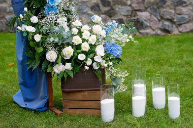 Açık havada düğün için bir yer. Mavi kumaş, çiçek aranjmanı ve mumlarla süslenmiş ahşap bir kemer. Yumuşak seçici odak.