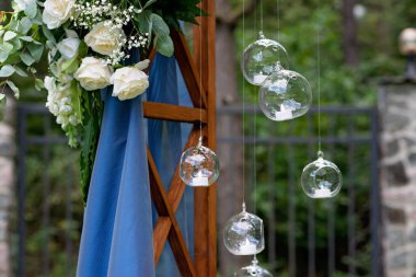 Açık havada düğün için bir yer. Mavi kumaş, çiçek aranjmanı ve mumlarla süslenmiş ahşap bir kemer. Yumuşak seçici odak.