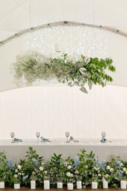 Restoranda düğün başkanlığı. Çiçekleri, yeşilliği, mumları ve çelenkleri olan yeni evliler için ziyafet masası. Çiçek aranjmanı. Lüks düğün süslemeleri. Yumuşak seçici odak.