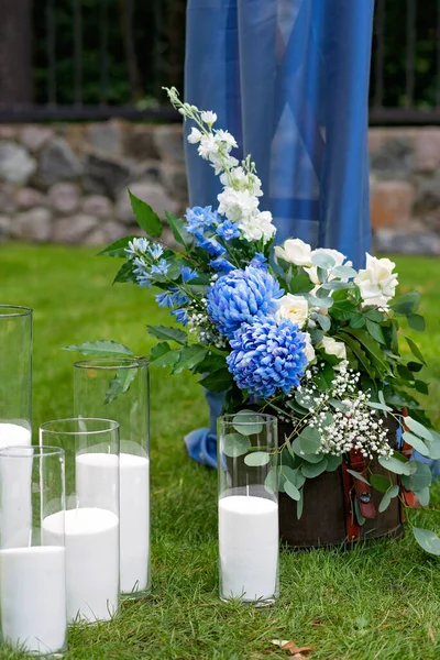 Açık havada düğün için bir yer. Mavi kumaş, çiçek aranjmanı ve mumlarla süslenmiş ahşap bir kemer. Yumuşak seçici odak.