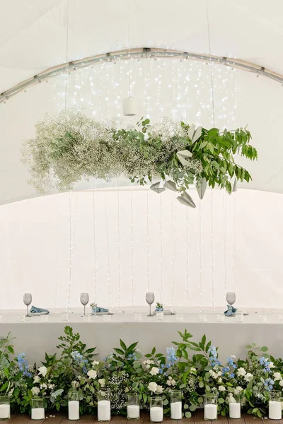 Restoranda düğün başkanlığı. Çiçekleri, yeşilliği, mumları ve çelenkleri olan yeni evliler için ziyafet masası. Çiçek aranjmanı. Lüks düğün süslemeleri. Yumuşak seçici odak.