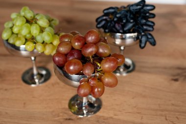 A bunch of blue, green and red grapes in metal bowls on a wooden table. Food, healthy eating. Soft selective focus.