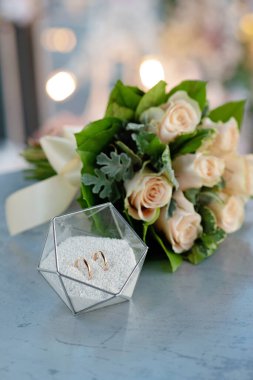 Modern cam bir stantta bir çift güzel alyans ve narin bir buket gül. Evlilik, tören. Yumuşak seçici odak.