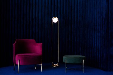 Rahat kırmızı kadife koltuklu bir daire, minimalist bir lamba ve koyu mavi kadife duvar panelleri ve zemin döşemesi olan bir odada yeşil bir pouffe. Lüks iç tasarım kavramı.