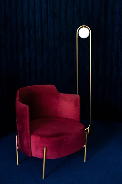 A room with a comfortable red velor armchair, a minimalist floor lamp in the living room with dark blue velvet wall panels and floor carpeting.