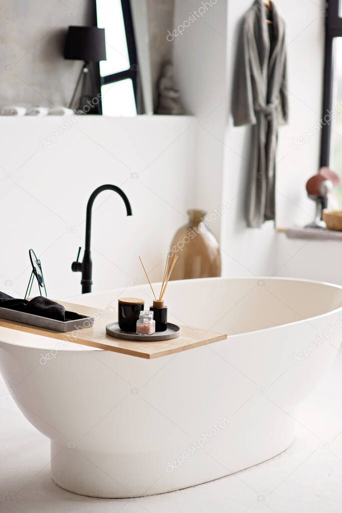 Empty white bathtub in modern apartment with stylish loft style interior design, home decor. Spa concept, relaxation. Soft selective focus.