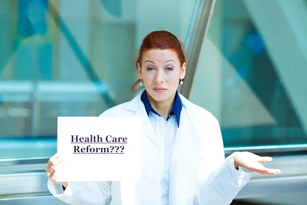 Confused doctor holding health care reform???sign — Stock fotografie