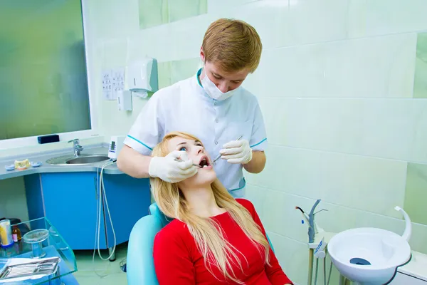 Dentista examinando paciente adulto jovem, fazendo a limpeza dos dentes — Fotografia de Stock