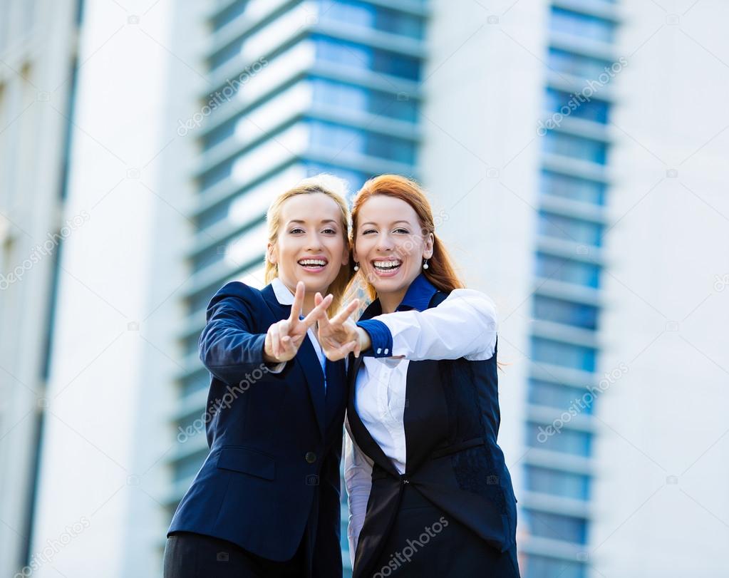 Two excited business women, friends giving victory sign, gesture