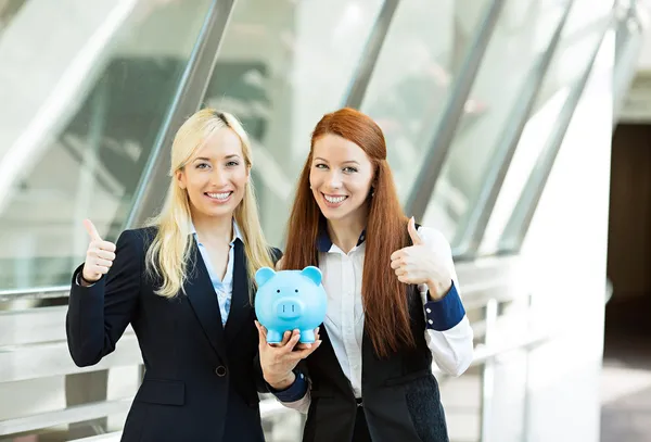 Portrait two happy business women holding piggy bank giving thum — Stock Photo, Image