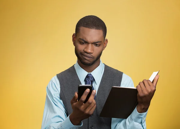 Skeptical man looking at phone holding book — Stock Photo, Image