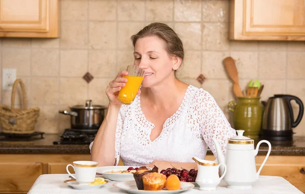 Μέσης ηλικίας γυναίκα έχοντας πρωινό σε μια κουζίνα — Φωτογραφία Αρχείου