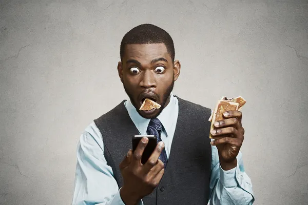 Impresionado hombre de negocios leyendo noticias de última hora en el teléfono mientras come —  Fotos de Stock