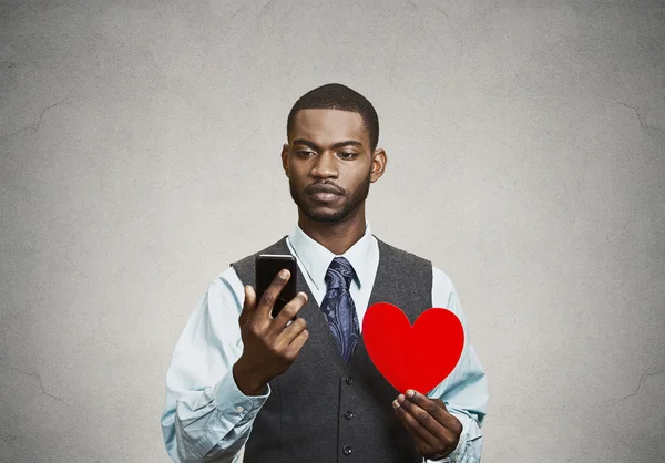 L'homme vérifie son téléphone intelligent, tenant son cœur rouge — Photo