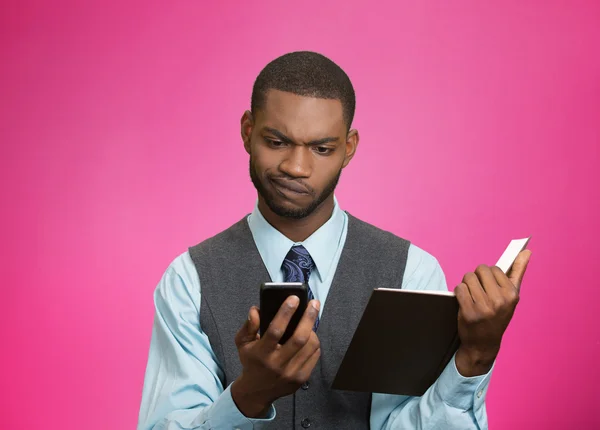 Skeptical man looking at phone holding book — Stock Photo, Image