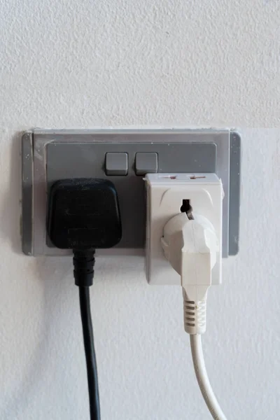 Close up of two electrical plugs from electrical appliances inserted into electrical outlets on the wall.