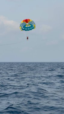 Yetişkin bir adam Maldivler 'de tropikal bir plaj tatilindeyken açık denizde paraşütle atlıyor..
