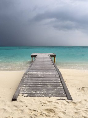Sahilden Maldivler 'deki bir adada, okyanusun turkuaz sularına giden boş bir ahşap iskele..