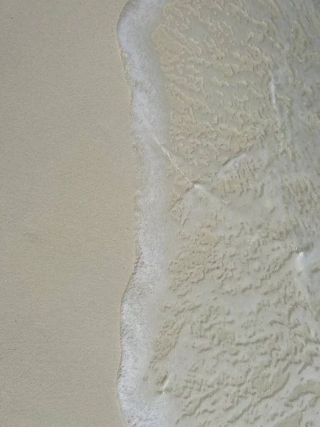 A vertical view of a frothy white wave washing on white sandy beach on an island in the Maldives.