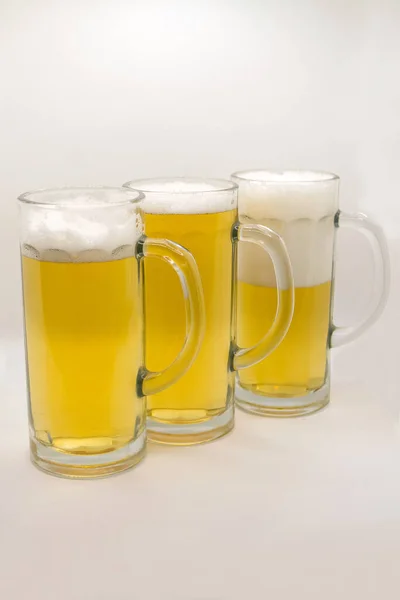 Três canecas de vidro com cerveja em um fundo branco — Fotografia de Stock