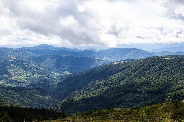 Yeşil ve mavi dağ manzarası. Sıcak, güneşli bir yaz gününde, beyaz bulutlu ve mavi gökyüzü olan bir arka plan. Avrupa dağları ve seyahat kavramı