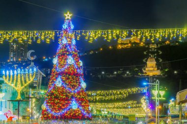 Hayfa, İsrail - 01 Aralık 2021: Alman Kolonisinde Tatil Tatili, bir Noel ağacı, Hanuka Menorah, Müslüman Hilal ve arka planda İsrail 'in Hayfa kentindeki Bahai türbesi
