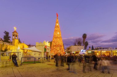 Nasıra, İsrail - 24 Aralık 2021: Nazareth, İsrail 'deki Yunan Ortodoks Annunciation Kilisesi, Noel ağacı ve kalabalıkla birlikte kilise meydanının akşam manzarası