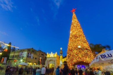 Nasıra, İsrail - 24 Aralık 2021: Nazareth, İsrail 'deki Yunan Ortodoks Annunciation Kilisesi, Noel ağacı ve kalabalıkla birlikte kilise meydanının akşam manzarası