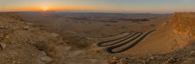 Güney İsrail 'in Negev Çölü' ndeki Makhtesh (krater) Ramon 'un dolambaçlı bir yolun panoramik gündoğumu manzarası. Büyük bir erozyon sirkinin jeolojik bir alanı.