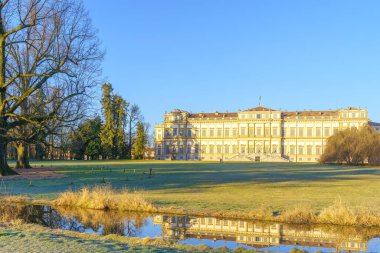 View of the Villa Reale building, with lawn, trees, and water stream, in the Monza Park, on a clear winter day. Monza, Lombardy, Northern Italy