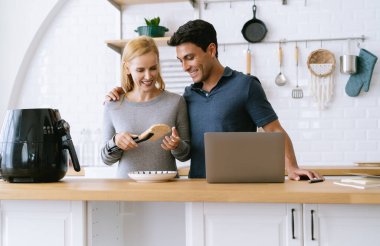 Mutfakta çekici orta yaşlı bir çift. Güzel kadın Air Fryer makinesinin yanında tost pişirirken yakışıklı adam dizüstü bilgisayarla çalışıyor. Evden çalışmak, Yeni Normal Kavram.