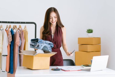 Güzel bayan girişimci Asyalı gelişigüzel kadın KOBİ küçük işletme siparişlerini kontrol ediyor ve karton kutudan müşteriye ürünleri paketliyor. Serbest çalışma, online iş fikirleri. KME pazarlama kavramı