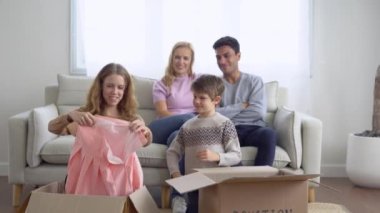Mutlu bir beyaz aile, kış günü evlerinde oturma odasında otururken eşyalarını karton kutuya koyup ihtiyaç sahiplerine bağış yapıyor. Bağış ve yardım konsepti.